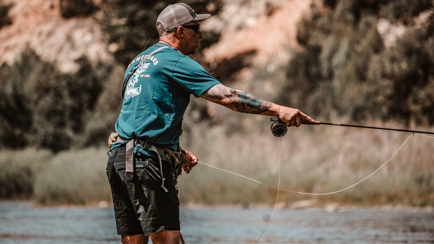 FISHING BOTTOMS. Fly fisherman wears GameGuard Travel Shorts while casting in river. Quick-dry fishing shorts, water-repellent, UPF 30+, lightweight stretch fabric, performance fishing bottoms, outdoor apparel, GameGuard angler gear, vented waistband.