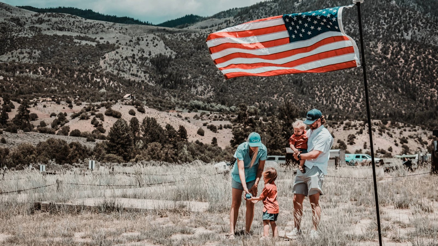 AMERICA COLLECTION. Family stands under US flag in GameGuard MeshBack Caps, performance outdoor shirts, and Travel Shorts. Patriotic outdoor apparel, red white & blue gear, GameGuard USA collection, UPF shirts, moisture-wicking, summer adventure clothing.