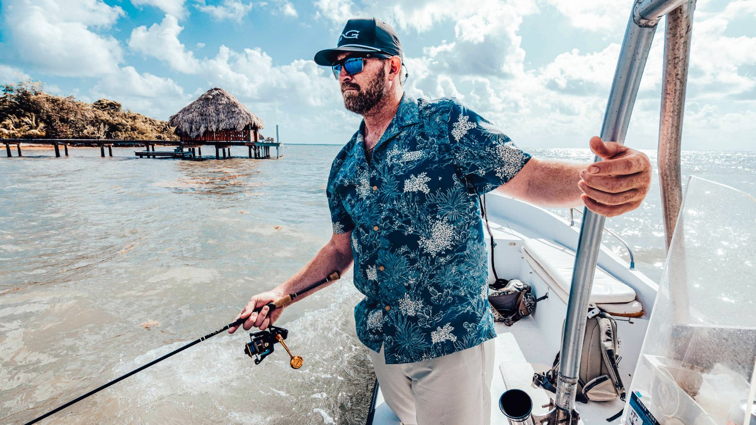 VOYAGER SHIRT. Man wears GameGuard Voyager Shirt in tropical print beside U.S. flag. Short sleeve button-up, casual travel shirt, coconut buttons, moisture-wicking, lightweight performance shirt, GameGuard island-style menswear, relaxed fit outdoor shirt.