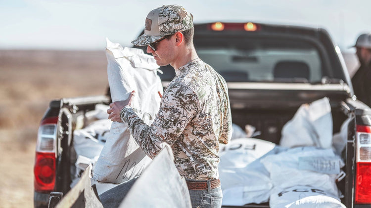 TRACKER TEE. Man unloads truck in GameGuard Digital Tracker Tee and camo MeshBack Cap. Long sleeve hunting tee, cotton blend, all-over camo, outdoor work shirt, concealed hunting shirt, GameGuard Digital camo tee, ranch wear, durable performance tee.