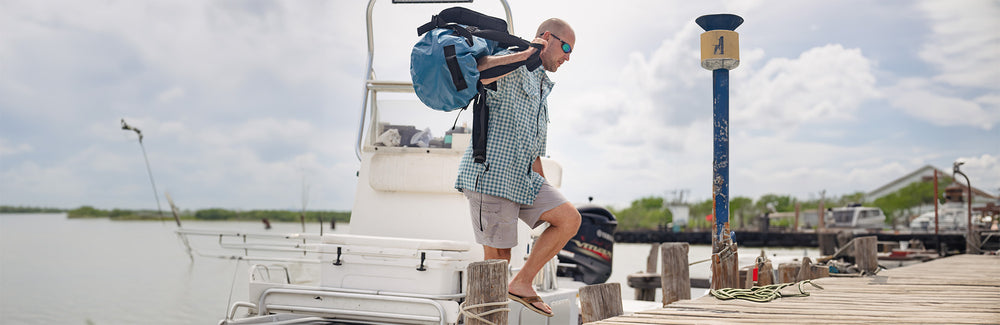 man carrying waterproof duffle bag, the Marine DryDuffle, after fishing on the water. Built for hunting and fishing