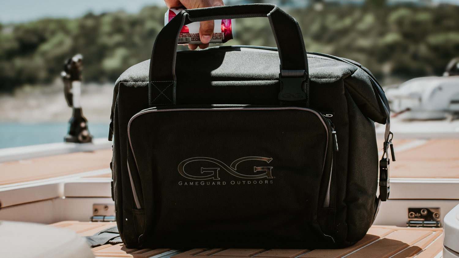 FIELD GEAR & COOLER BAGS. Two paddleboards rest on a wooded shoreline with paddles and GameGuard cooler bags on top, surrounded by dense green foliage and calm water.