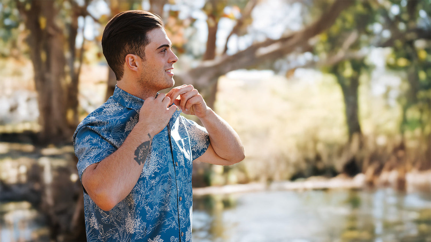 Man adjusting collar in a water and beach setting feeling relaxed wearing a Off-Road Blue Voyager Shirt