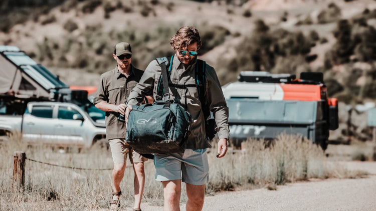 COOLER BAGS. Man carries GameGuard Cooler Bag in rugged outdoor setting. Insulated cooler bag, 36-can capacity, welded seams, leakproof liner, padded strap, GG field gear, outdoor adventure bag, hunting cooler, camping gear, soft cooler, durable design.