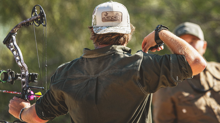 FLANNEL. Archer wears GameGuard Flannel Shirt with deep green tone and rugged stitching. Outdoor flannel shirt, hunting shirt, UPF 50+, western flannel, active fit, concealed pocket, GameGuard gear, cool-weather layering shirt, archery-ready apparel.