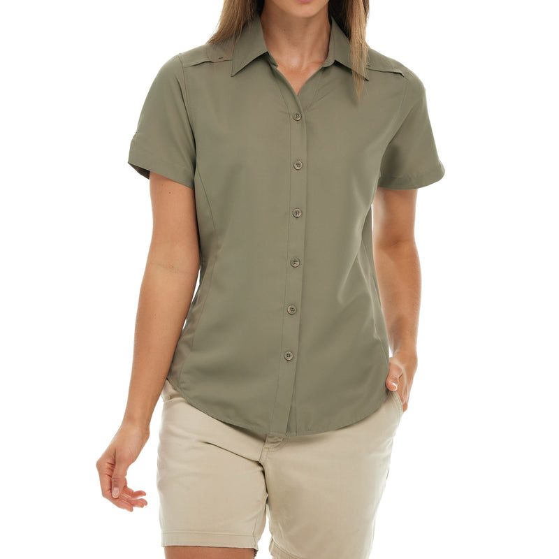 Load image into Gallery viewer, Front view of a woman wearing the Mesquite Ladies&#39; Shirt, a short-sleeve shirt with microfiber fabric in green, with her hands in the pockets of her shorts. Tailored fit for comfort and style.
