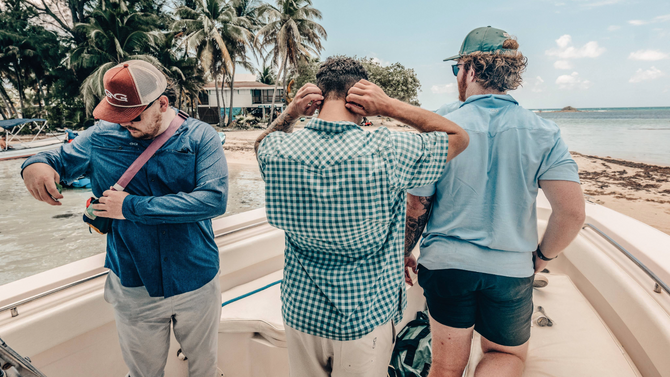 Three men on a boat near the beach wearing blue fishing shirts 