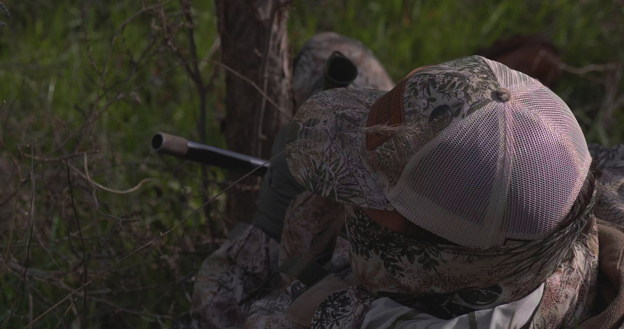 Man sitting wearing GameGuard Hunting Apparel, Jacket, Pants, Bino Case, Cap, and Gaiter, using his turkey call to hunt turkeys.